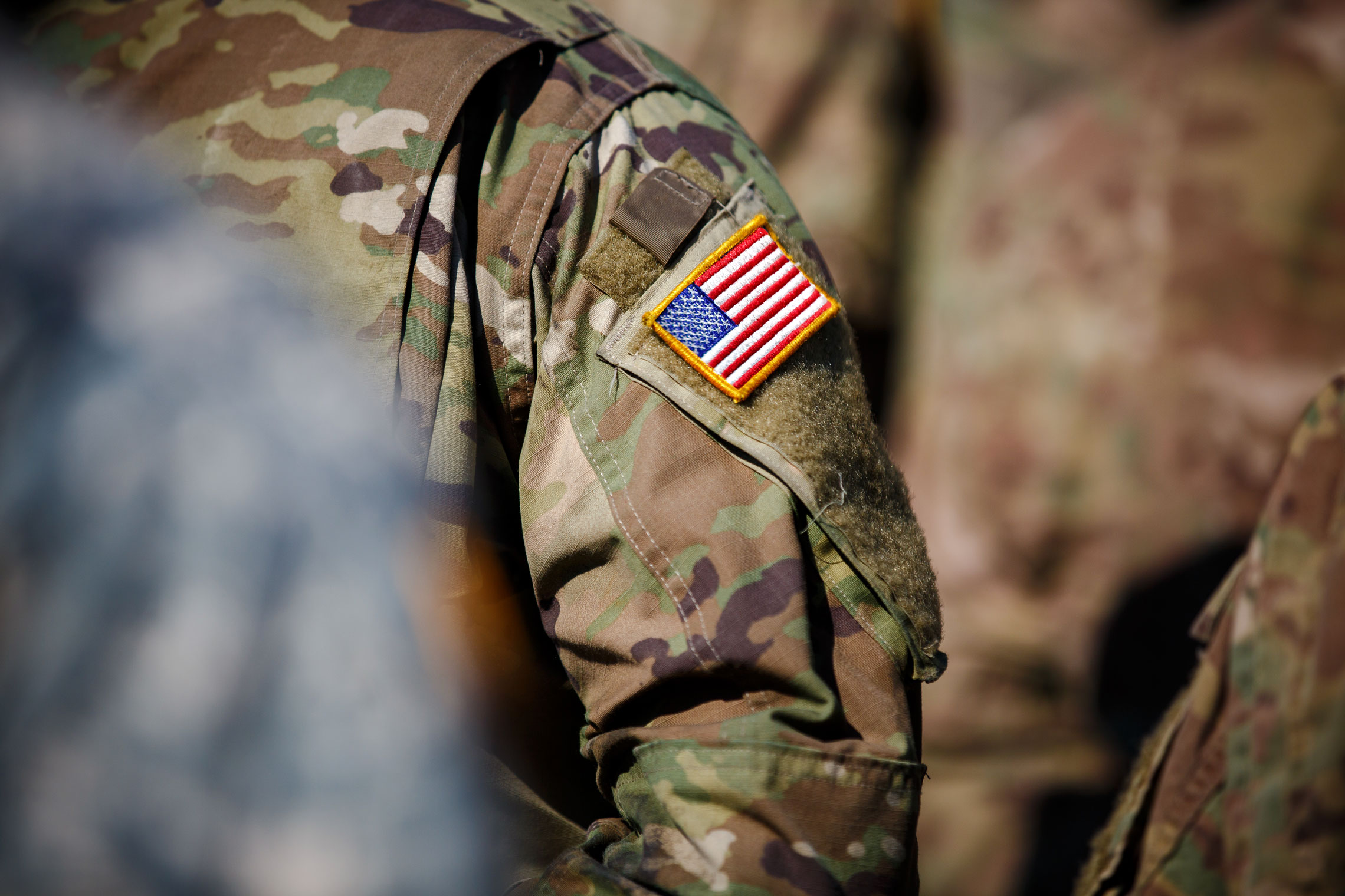 Close-up of a U.S. Army soldier’s camouflage uniform with an American flag patch in focus on the shoulder.